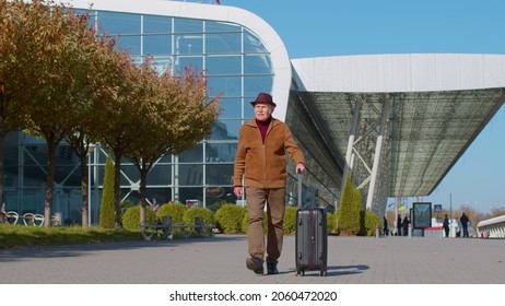 Elderly old retired grandpa tourist go to international airport terminal for boarding on plane for traveling. Stylish senior mature grandfather carrying luggage suitcases on wheels to railway station