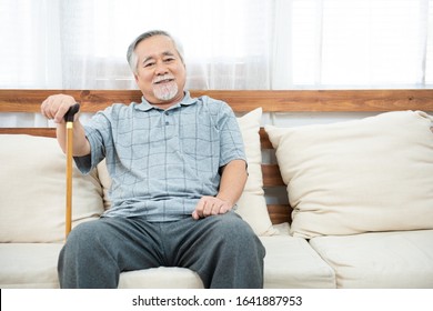 elderly old senior man sitting, resting his hands on wooden walking stick sitting on couch in living room in house after retirement. - Powered by Shutterstock