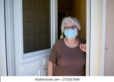 Elderly Old Senior Woman Opening Front Door Of House And Welcoming People At Home Wearing A Surgical Mask To Avoid Covid19 And Coronavirus Contamination