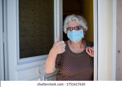 Elderly Old Senior Woman Opening Front Door Of House And Welcoming People At Home Wearing A Surgical Mask To Avoid Covid19 And Coronavirus Contamination