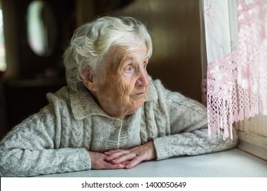 An Elderly Old Woman Looks Sadly Out The Window. Care For Lonely Pensioners.