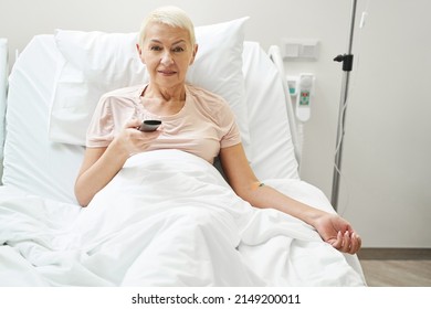 Elderly Patient Clicking TV Remote While Under Intravenous Therapy