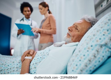 Elderly patient recovering in the hospital ward while his daughter is communicating with a doctor in the background. - Powered by Shutterstock