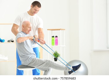 Elderly patient training with rubber band under doctor's supervision in physiotherapy center - Powered by Shutterstock