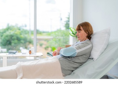 Elderly Patient Woman Lying On Bed Wearing Broken Arm Support At Hospital. Feeling Lonely And Hurt Arm Broken. Healthcare And Insurance Concept. Injured Woman Pain On Arm After Treatment