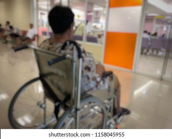 Elderly Patients Sitting On Wheelchair Waiting For The Doctor In Front Off Emergency Room, At Hospital, With Space For Text, Blur Background. Selective Focus.