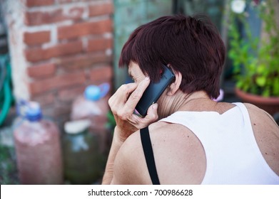 An Elderly Pensioner Is Talking On The Phone On The Street. Grandma Is Holding The Phone. The Grandmother In A White Jersey Calls By A Black Phone.