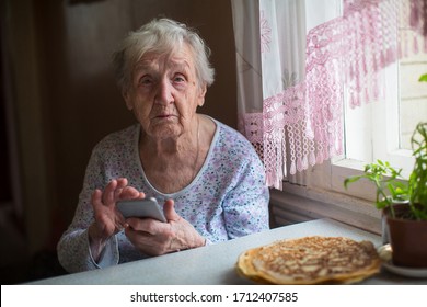 Elderly pensioner woman sits with a smartphone in her home.