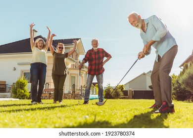 Elderly People Having Fun Playing Mini Golf At The Backyard Lawn, Spending Sunny Summer Day Outdoors