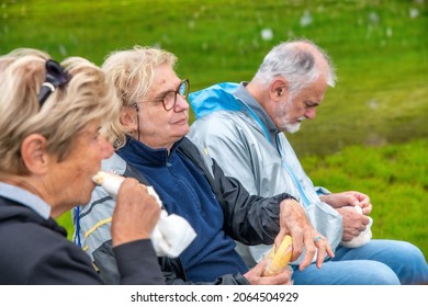 Elderly people relaxing at the end of a mountain hike, eating sandwiches on the grass - Powered by Shutterstock