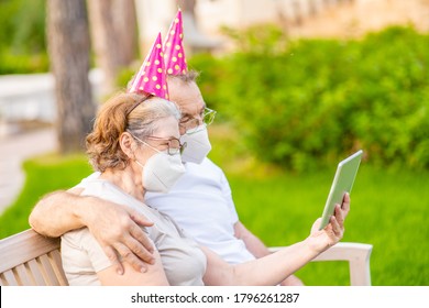 Elderly people wearing party's caps and protective face masks celebrates  birthday with her family on video call during the coronavirus epidemic - Powered by Shutterstock