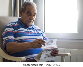 Elderly Person Looking At A Calendar Sitting In An Armchair Next To A Very Bright Window With A Striped Shirt