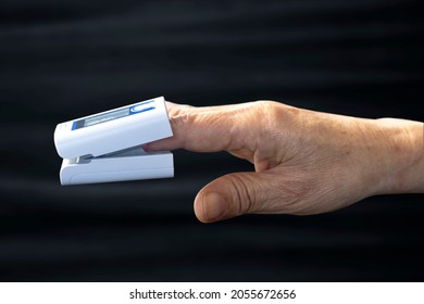 Elderly Person's Finger And Pulse Oximeter Seen From The Side, Black Background