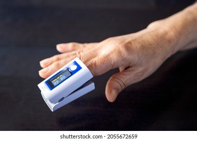 Elderly Person's Finger And Pulse Oximeter Seen From An Angle, Black Background