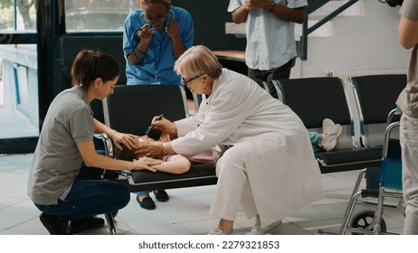 Elderly physician consulting small unconscious child with flashlight, doing checkup in health center lobby. Doctor trying to help young kid with illness, fainting on chairs in hospital reception. - Powered by Shutterstock