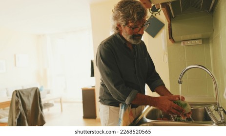 Elderly positive man washing vegetables in the kitchen - Powered by Shutterstock