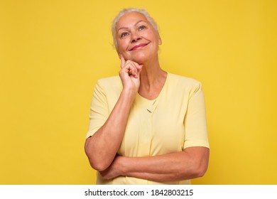 Elderly pretty woman standing daydreaming or reminiscing looking up. Studio shot on yellow wall. - Shutterstock ID 1842803215