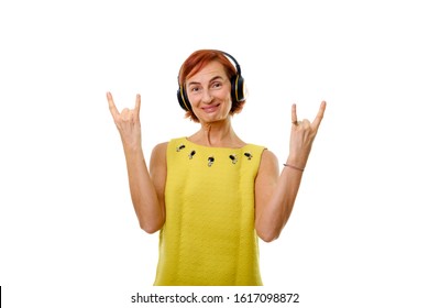 Elderly Redhead Woman 55-60 Years Old Dressed Casually Standing With Smile Expression, Listening To Music In Headphones And Showing Rock Sign. Concept Of Lifestyle, Music, Fun. Isolated On White. 