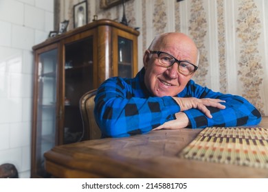 Elderly retired caucasian grandfather resting his arms on a wooden table looking at camera and smiling. Old-fashioned interior. Happy retirement concept. High quality photo - Powered by Shutterstock