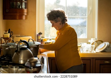 Elderly retired gray-haired woman having a good time in her house, active in her old 80 age, washing dishes in a cozy kitchen, cleaning. A happy grandmother in a smart yellow blouse, young at heart. - Powered by Shutterstock