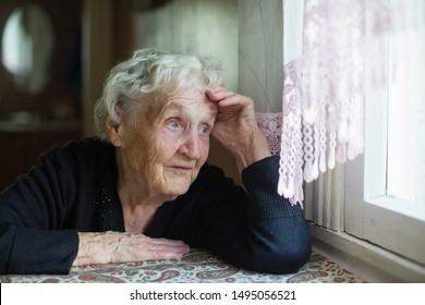 Elderly Russian Woman Sits In A House Near The Window. 