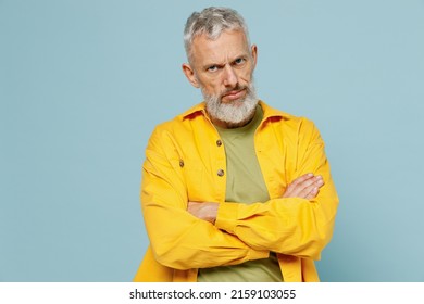 Elderly sad offended indignant shrewd gray-haired mustache bearded man 50s wear yellow shirt hold hands crossed folded isolated on plain pastel light blue background studio. People lifestyle concept