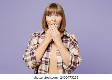 Elderly sad scared sad astonished gray-haired woman 50s years old wearing beige t-shirt shirt casual clothes cover mouth with hand isolated on plain pastel light purple background. Lifestyle concept