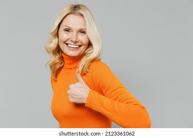 Elderly Satisfied Happy Smiling Happy Blonde Caucasian Woman 50s In Orange Turtleneck Showing Thumb Up Like Gesture Isolated On Plain Grey Color Background Studio Portrait. People Lifestyle Concept