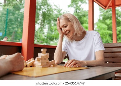 elderly senior couple playing board game and building a tower with wooden bricks outdoors in the park, old woman shows facepalm and loses by making a mistake in jenga - Powered by Shutterstock