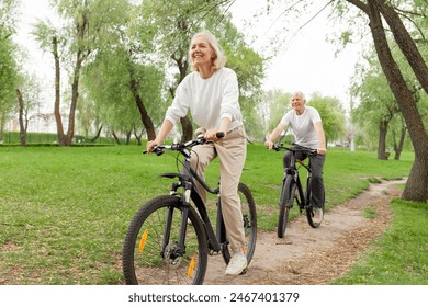 elderly senior couple rides bicycle in the park in the summer and smiles, old gray-haired man and woman are actively resting outdoors, old people practice cycling in forest - Powered by Shutterstock