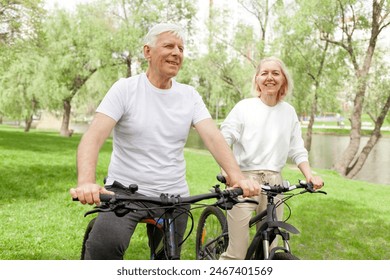 elderly senior couple rides bicycle in the park in the summer and smiles, old gray-haired man and woman are actively resting outdoors, old people practice cycling in forest - Powered by Shutterstock