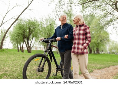 elderly senior couple rides bicycle in the park in the summer and smiles, old gray-haired man and woman are actively resting outdoors, old people practice cycling in forest - Powered by Shutterstock