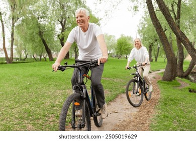 elderly senior couple rides bicycle in the park in the summer and smiles, old gray-haired man and woman are actively resting outdoors, old people practice cycling in forest - Powered by Shutterstock