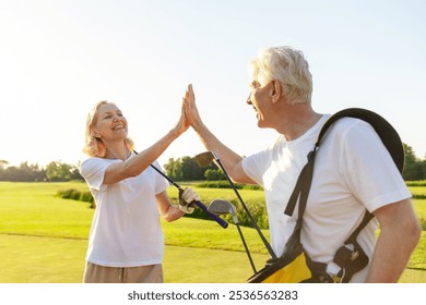 elderly senior couple in uniform celebrating victory and success in golf game and giving high five, old man and woman playing golf on golf course at sunset and doing outdoor sports - Powered by Shutterstock