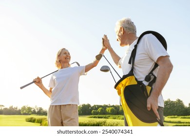 elderly senior couple in uniform celebrating victory and success in golf game and giving high five, old man and woman playing golf on golf course at sunset and doing outdoor sports - Powered by Shutterstock