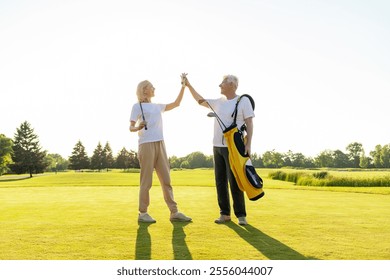 elderly senior couple in uniform celebrating victory and success in golf game and giving high five, old man and woman playing golf on golf course at sunset and doing outdoor sports - Powered by Shutterstock