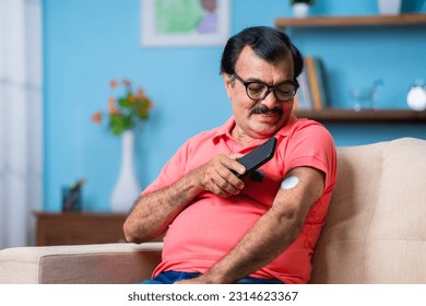 Elderly senior man checking glucose level by tapping smartphone to monitoring sensor at home - concept of health care, technology and mdicare.