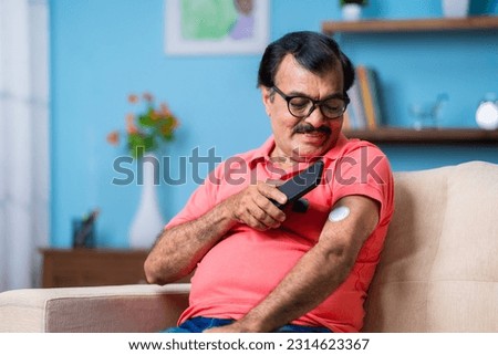 Elderly senior man checking glucose level by tapping smartphone to monitoring sensor at home - concept of health care, technology and mdicare.