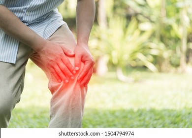 Elderly Or Senior Man Hands Hold On His Knee Or Suffering From Pain In Knee While Exercise At Backyard. Injury, Knee Pain, Man With Legs Ache Concept. Shot In Morning Time. Highlight Red Effect 