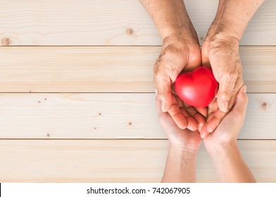 Elderly Senior Person Or Grandparent's Hands With Red Heart  In Support Of Nursing Family Caregiver For National Hospice Palliative Care And Family Caregivers Month Concept