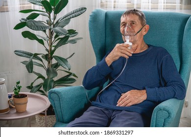 An elderly senior sits in a armchair with an oxygen mask in quarantine at home