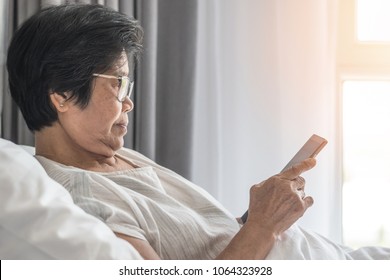 Elderly Senior Woman Aged Person Lifestyle Using Mobile Tablet And Digital Internet Technology Reading E-book, Social Media Network On Bed In Nursing Home Or Health Care  