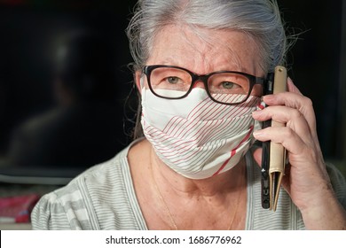 Elderly senior woman with glasses wearing hand made cotton mouth nose virus face mask, talking over her phone. Coronavirus covid-19 outbreak prevention concept