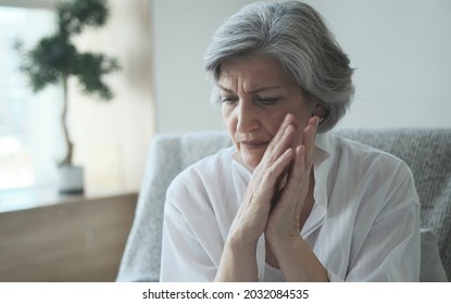 Elderly senior woman massaging her temples to reduce her headache. Older lady feeling scared, anxious, and thinking of sickness or mental health while suffering from a severe migraine or memory loss.