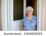 elderly senior woman opening front door of house and welcoming people at home 