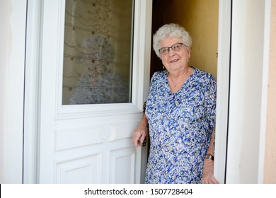 Elderly Senior Woman Opening Front Door Of House And Welcoming People At Home 