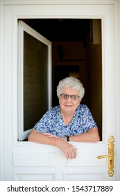 Elderly Senior Woman Opening Front Door Of House And Welcoming People At Home 