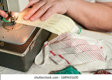 Elderly Senior Woman Working On Old Sewing Machine - Making Home Made Face Masks Against Coronavirus Spreading, Closeup Detail Pile Of Finished Mask