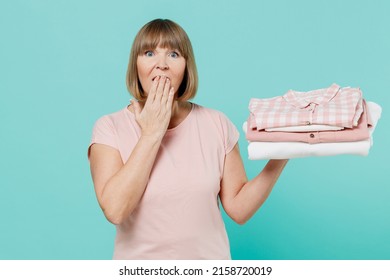 Elderly Shocked Amazed Housewife Woman 50s In Pink T-shirt Doing Housework Hold Pile Of Ironed Clothes Isolated On Plain Pastel Light Blue Background Studio. Housekeeping Cleaning Tidying Up Concept