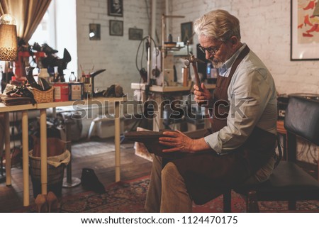 An elderly shoemaker in an apron at work